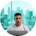 Tech founder portrait in a glass-walled office with a laptop and city skyline behind him